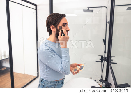 Focused young man standing in the bathroom during makeup application 99023465