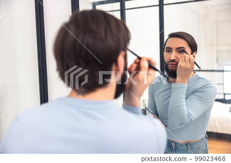 Focused male putting on eye cosmetics before the mirror 99023468