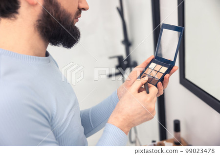 Adult man using a thin brush for blending eye shadows Adult man using a thin brush for blending eye shadows 99023478