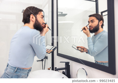 Serious concentrated young man using eye cosmetics 99023485