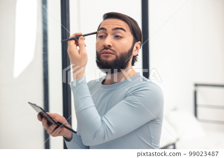 Transgender person applying the eyeshadows to his upper eyelid 99023487