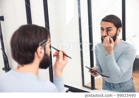 Guy applying eye cosmetics before the mirror 99023490