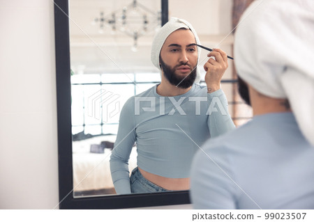 Cute young man pencilling brows in the bathroom 99023507