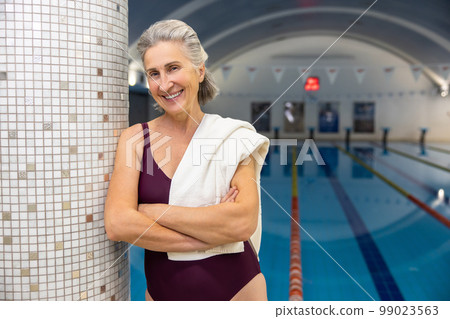 Smiling senior woman standing at the swimming pool with a towel on shoulder 99023563