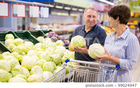 Mature family of retirees examines head of cabbage in grocery section of the supermarket 99024947