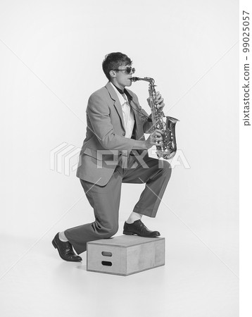 Live performance. Monochrome. Young stylish man playing saxophone. Concept of creativity, retro fashion style, music lifestyle. Black and white portrait 99025057