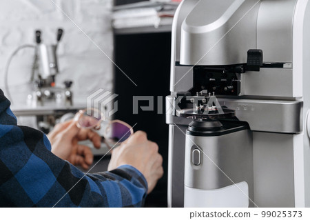 Optician's hands holding eyeglasses in professional workshop 99025373