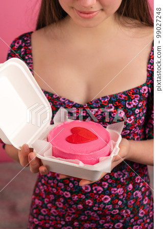 Close-up of bento cake with heart on top in female hands 99027248