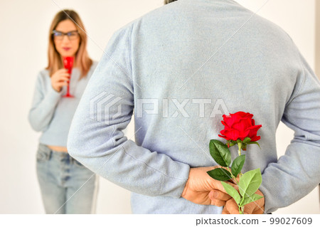 A man holding a red rose behind his back . A man holding a red rose behind his back . 99027609