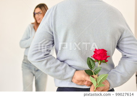 A man holding a red rose behind his back . A man holding a red rose behind his back . 99027614
