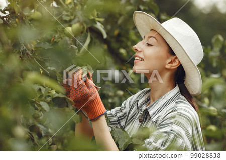 Young woman taking care of plants. Brunette in a hat and gloves. 99028838