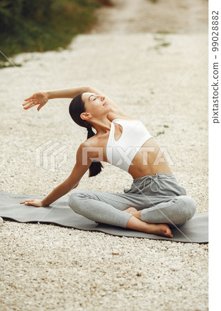 Pretty lady training on a summer beach. Brunette doing yoga. Girl in a sportsuit. 99028882