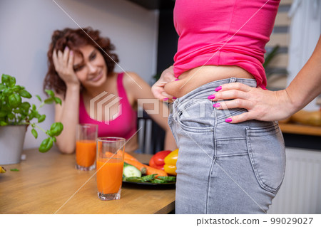 Woman squeezes the skin on her abdomen between her fingers assessing the amount of fat 99029027