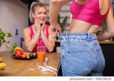 woman admires her friend's weight loss results while in the kitchen 99029028