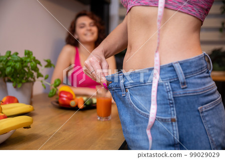 A woman shows off the effects of weight loss by stretching the waistband of loose pants. A woman shows off the effects of weight loss by stretching the waistband of loose pants. 99029029