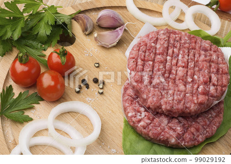 Raw Ground beef meat Burger steak cutlets on a wooden board background. Cutlet for burger with vegetables and spices. 99029192