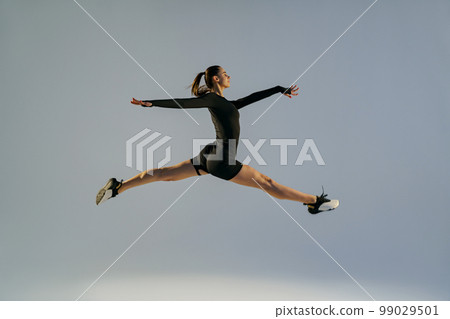 Sporty girl jumping doing split leap in air with joyful expression. Flexible and weightless concept Sporty girl jumping doing split leap in air with joyful expression. Flexible and weightless concept 99029501