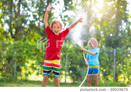 Kids play with water sprinkle hose. Summer garden 99029678