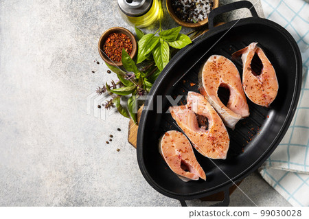 Pieces of fresh salmon fillet with spices on a grill pan. Seafood, culinary background. View from above. Copy space. Pieces of fresh salmon fillet with spices on a grill pan. Seafood, culinary background. View from above. Copy space. 99030028