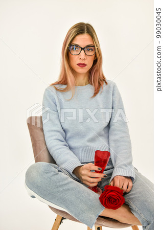 Young girl sitting on a chair holding a fresh red rose in her hand.  99030045