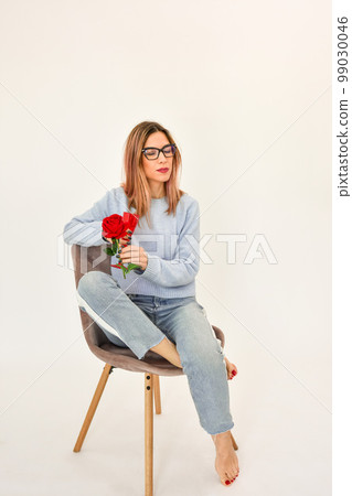 Young girl sitting on a chair holding a fresh red rose in her hand.  99030046