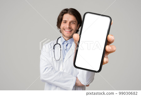 Handsome Male Doctor In Uniform Holding Big Blank Smartphone With White Screen Handsome Male Doctor In Uniform Holding Big Blank Smartphone With White Screen 99030682