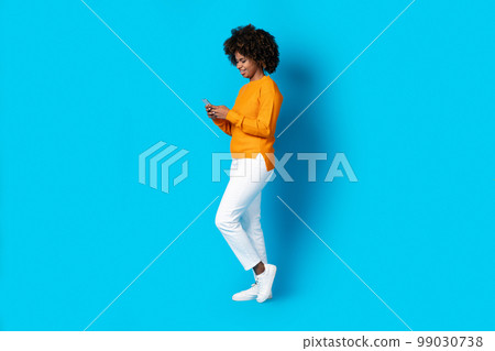 Black woman using cell phone on blue studio background 99030738