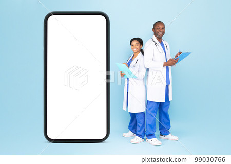 Telehealth concept. Happy male and female doctors in uniform standing near huge blank smartphone, mockup Telehealth concept. Happy male and female doctors in uniform standing near huge blank smartphone, mockup 99030766