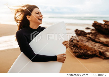 Happy lady in swimsuit holding surfboard under arm, going to have surfing training on ocean, sea background Happy lady in swimsuit holding surfboard under arm, going to have surfing training on ocean, sea background 99030857