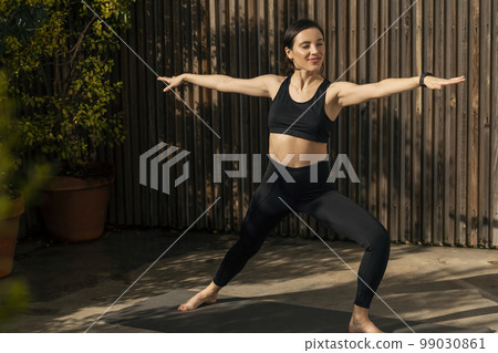 Smiling slim muscular caucasian millennial lady in sportswear practicing yoga, pilates, fitness outdoors 99030861