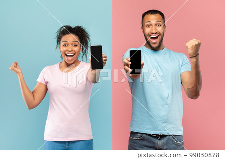 Yes. Happy black couple showing smarphones with blank screens and shaking clenched fists, mockup, banner Yes. Happy black couple showing smarphones with blank screens and shaking clenched fists, mockup, banner 99030878