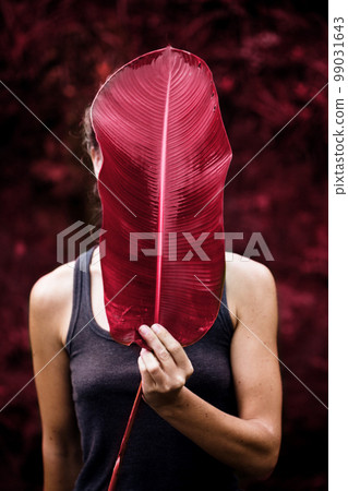 The girl covers her face with a large leaf, toned in pink The girl covers her face with a large leaf, toned in pink 99031643