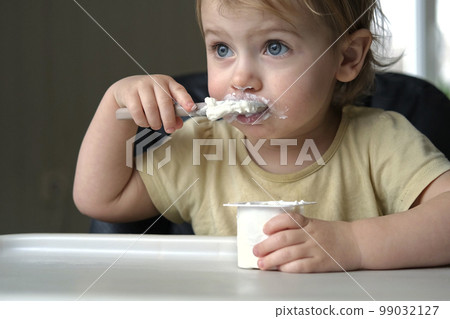 Young Kid Eating Blend Mashed Feed Sitting in High Chair. Baby Weaning. Little Girl Learning to Eat Yogurt, Feeding Himself. Small Hand with Spoon. Breakfast with Dairy Product. Child First Solid Food Young Kid Eating Blend Mashed Feed Sitting in High Chair. Baby Weaning. Little Girl Learning to Eat Yogurt, Feeding Himself. Small Hand with Spoon. Breakfast with Dairy Product. Child First Solid Food 99032127