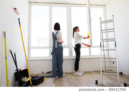 Young caucasian women, sisters or friends cleaning window together in room. Young caucasian women, sisters or friends cleaning window together in room. 99032700