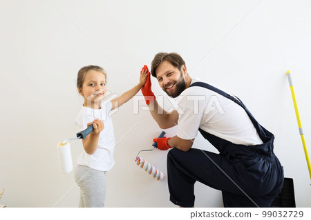Father and his cute child daughter standing and paints the wall with white paint giving high five 99032729