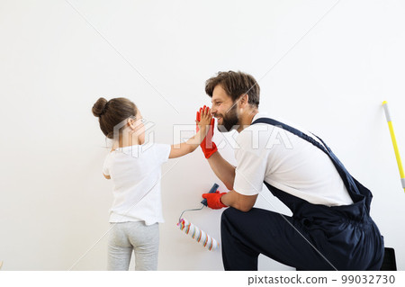 Father and his cute child daughter standing and paints the wall with white paint giving high five 99032730