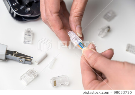 A woman's hand inserts an internet cable into a clamp connector. utp ethernet network cable plug. The concept of internet communications. A woman's hand inserts an internet cable into a clamp connector. utp ethernet network cable plug. The concept of internet communications. 99033750