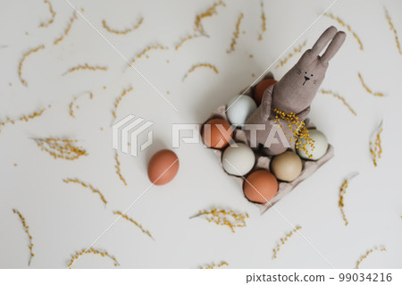 Funny handmade bunny rabbit toy with colorful chicken eggs and yellow mimosa flowers. Easter gift concept 99034216