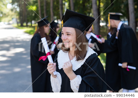 Group of happy students in graduation gowns outdoors. A young girl is happy to receive her diploma. 99034446