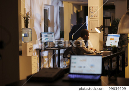 Advisor agent standing at desk table analyzing marketing statistics on computer, working at company strategy late at night in startup office. Executive manager planning investment graph 99034609