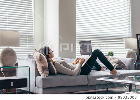 Woman watching tv movie on laptop lying on sofa Woman watching tv movie on laptop lying on sofa 99035008