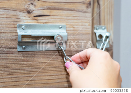 Close up of hand holding security door chain on wooden door Close up of hand holding security door chain on wooden door 99035258