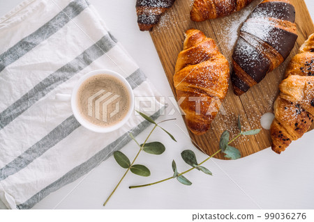 Cup of cappuccino with kitchen towel and eucalyptus branch, brown croissants on the cutting board 99036276