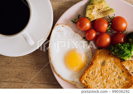 Close up homemade breakfast with cup of black coffee, fried egg and toast with tomatoes and avocado on a plate Close up homemade breakfast with cup of black coffee, fried egg and toast with tomatoes and avocado on a plate 99036292