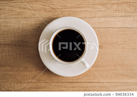 Flat lay black coffee in a white cup with a saucer on a wooden table Flat lay black coffee in a white cup with a saucer on a wooden table 99036334