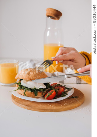 Breakfast sandwich with egg and arugula and cherry tomatoes on the table with orange juice 99036444
