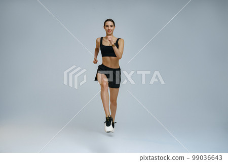 Sporty determined woman wearing sportswear running during cardio workout over studio background Sporty determined woman wearing sportswear running during cardio workout over studio background 99036643