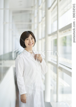 A smiling young woman in a white coat looking at the camera portrait 99038501