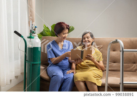 Caregiver takecare elderly woman while wearing oxygen nasal cannula at home. 99038891