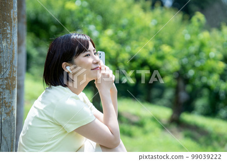 一個在新鮮的綠色公園裡聽智能手機音樂的女人 一個在新鮮的綠色公園裡聽智能手機音樂的女人 99039222